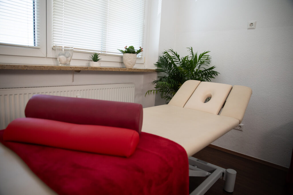 Weiße Liege mit rotem Handtuch und Kopfpolster in einem Behandlungsraum der Physiotherapie am Dom